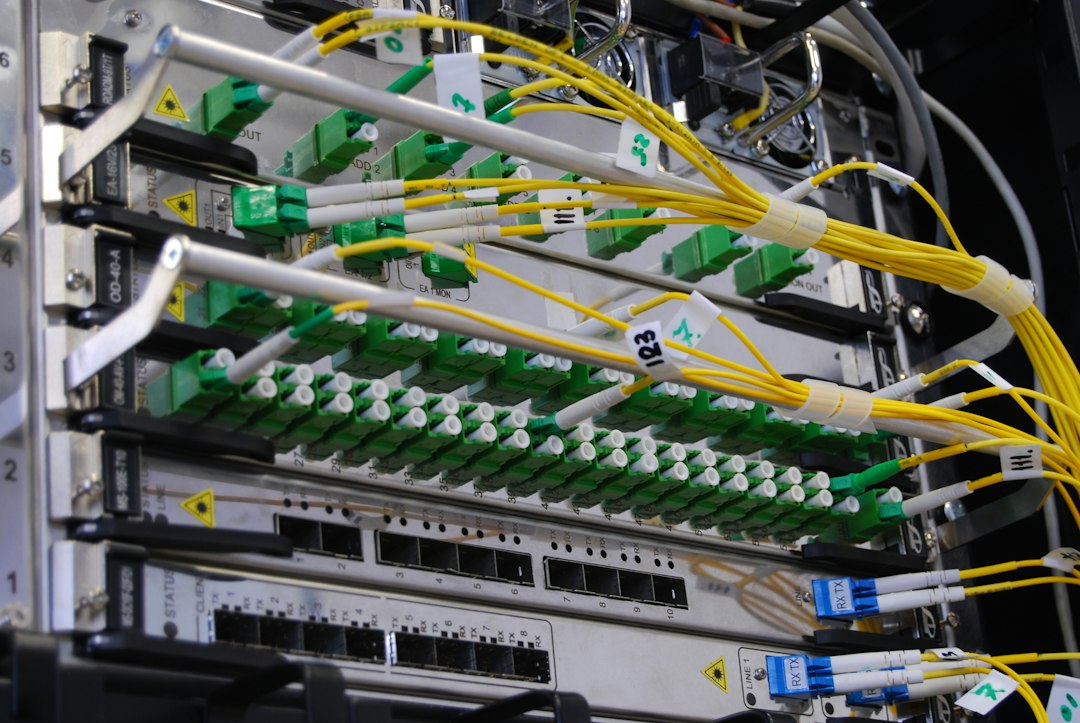 Detalhe de um rack de servidores com conectores de fibra verdes e cabos de rede amarelos.