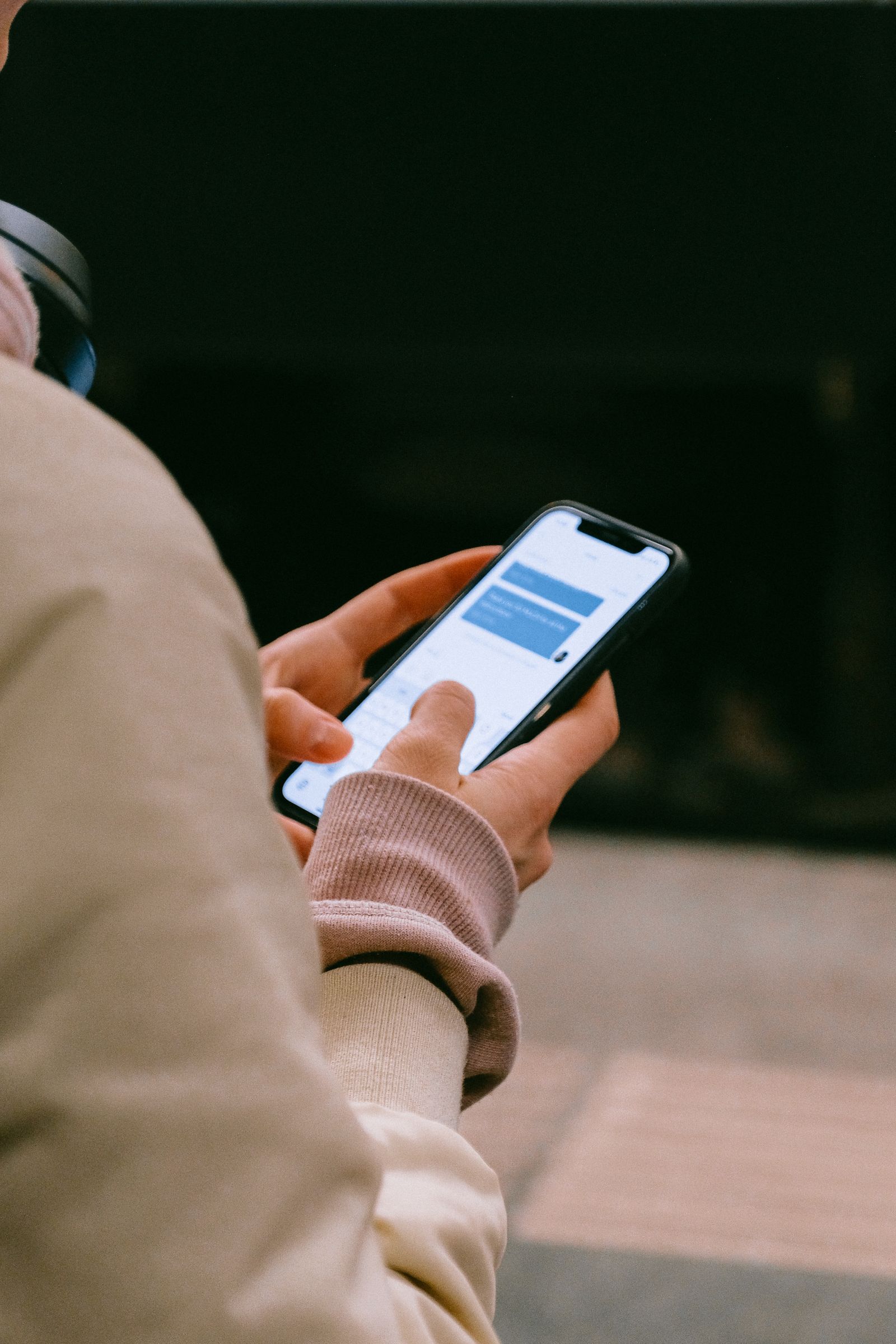 Mãos segurando um smartphone com uma tela de mensagens, ao ar livre.